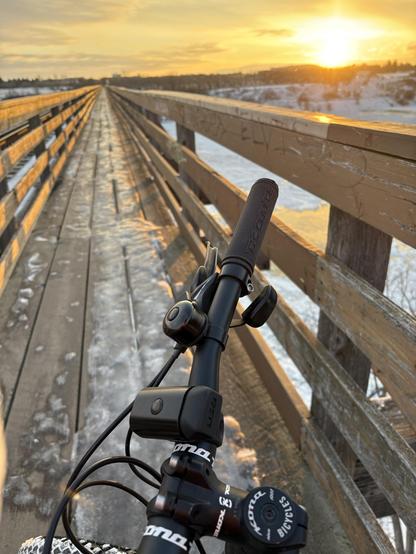 An icy narrow wooden bridge over a river in front of a yellow sunrise