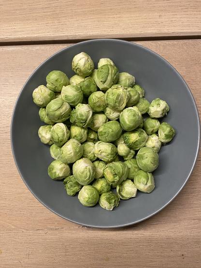 Geputzte Rosenkohlröschen in einem blauen Suppenteller auf einem hellen Holztisch