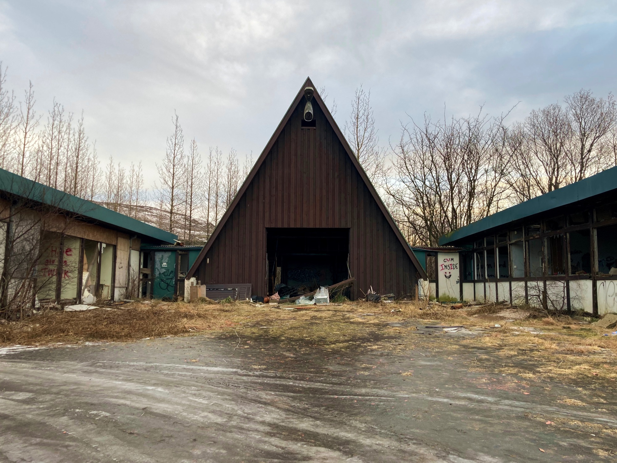 An abandoned A-frame building surrounded by trees in the winter.