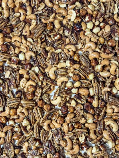 A tray of pecans, hazelnuts, and cashews, lightly golden brown and slightly glistening with a candy coating. You can see each nut's discinct color.