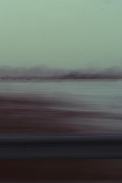 Color photo taken semi-randomly out the passenger window while driving the skyway from illinois to indiana. In the lower part of the window, the guardrail keeping me out of the lake is visible. Above that, we see the embankment/shore in reddish hues. Above that, the lake and then the far shoreline and trees. The top third--the sky--is slightly green-tinted. The whole thing is heavily blurred in a left (the direction of car motion) to right fashion, resulting in a painterly, Impressionist look.