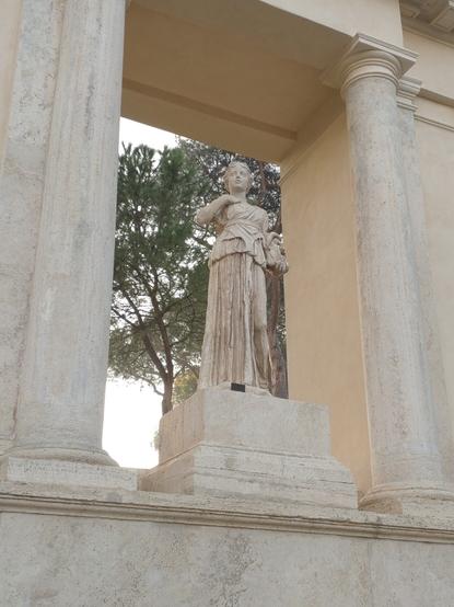 公園内の門のような構造物の中央に据えられた女性の彫像。古代のワンピースのような衣服をまとっている。右手を上げて喉のあたりに据えている。