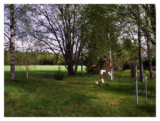 En liggande bild på en träfigur föreställande Zlatan Ibrahimovič i Milans dräkt. Framför hans fötter ligger en fotboll. Han står i en dunge av lövträd.