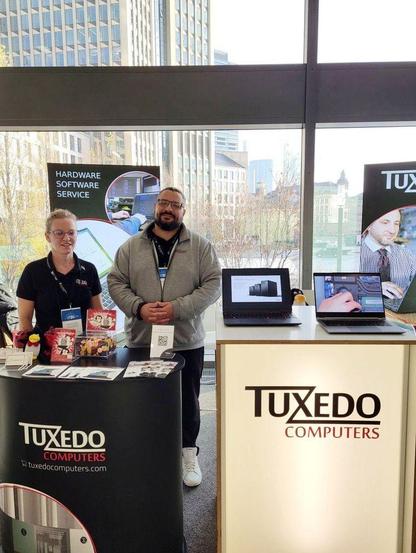 zwei leute am stand von tuxedo mit zwei aufgeklappten laptops.