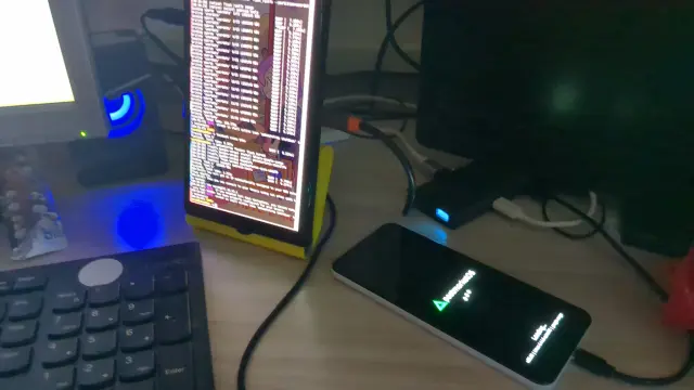 Фотография моего стола. Слева стоит вертикально нечто напоминающее планшет с кучей выводов команд бутстрапа (то есть, установщика постмаркета), а справа лежит подключенный к моей док-станции пиксель 3а белой модели, на нём виден треугольный логотип постмаркета и загрузочные точечки (анимация загрузки, в смысле, да, я странно такие вещи объясняю)