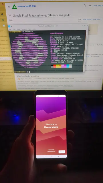 В кадре я держу в руках только что запустившийся телефон на линуксе, виден приветствующий экран графического окружения КДЕ плазма. На фоне 4 на 3 монитор, где я решила повыпендриваться и открыла терминал с выводом логотипа КДЕ Убунты на нинтендо свич через команду неофетч.