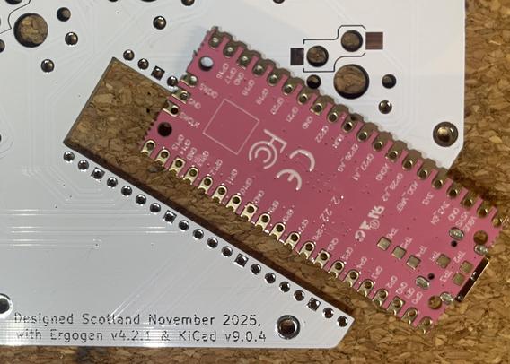 White #MechanicalKeyboard PCB with pink Raspberry Pi Pico controller laid on top face down, offset to show the cutout allowing it to be surface mounted with the components in the plane of the main PCB. Solder pads are missing (only on the other side - whoops).