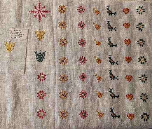 Borduurlinnen met rijen van verschillende geborduurde kerstfiguurtjes/-icoontjes (kleuren groen, geel en rood).