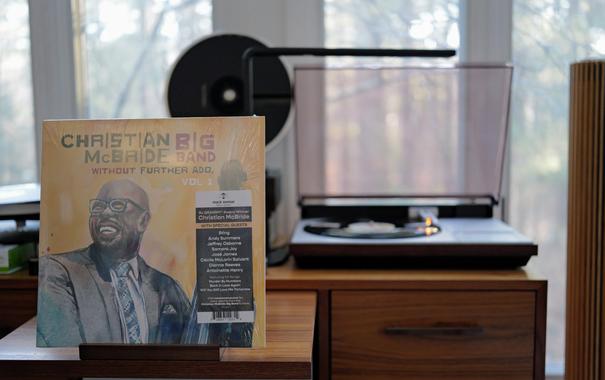Christian McBride Big Band - Without Further Ado, Vol. 1 LP cover.

A painting of Christian McBride, wearing a suit, holding his bass. Title and artist/group above.

The black LP plays on a vintage, restored Bang & Olufsen Beogram 4000 linear-tracking turntable to the right.