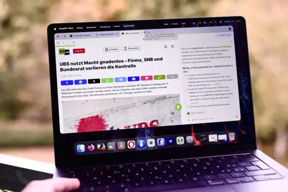 Laptop-Bildschirm zeigt einen Artikel mit dem Titel «UBS nutzt Macht gnadenlos – Finma, SNB und Bundesrat verlieren die Kontrolle» auf einer Webseite. Eine Hand hält den Laptop.
