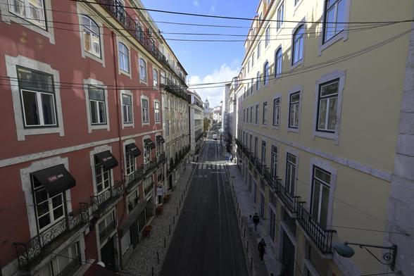 Eine Straße verläuft Vertikal durch das bild. Links und Rechts sind Häuserreihen zu sehen mit vielen Fenster. Links sind die Fassaden in eine Leberfarbe und Rechts in Blassgelb bemalt