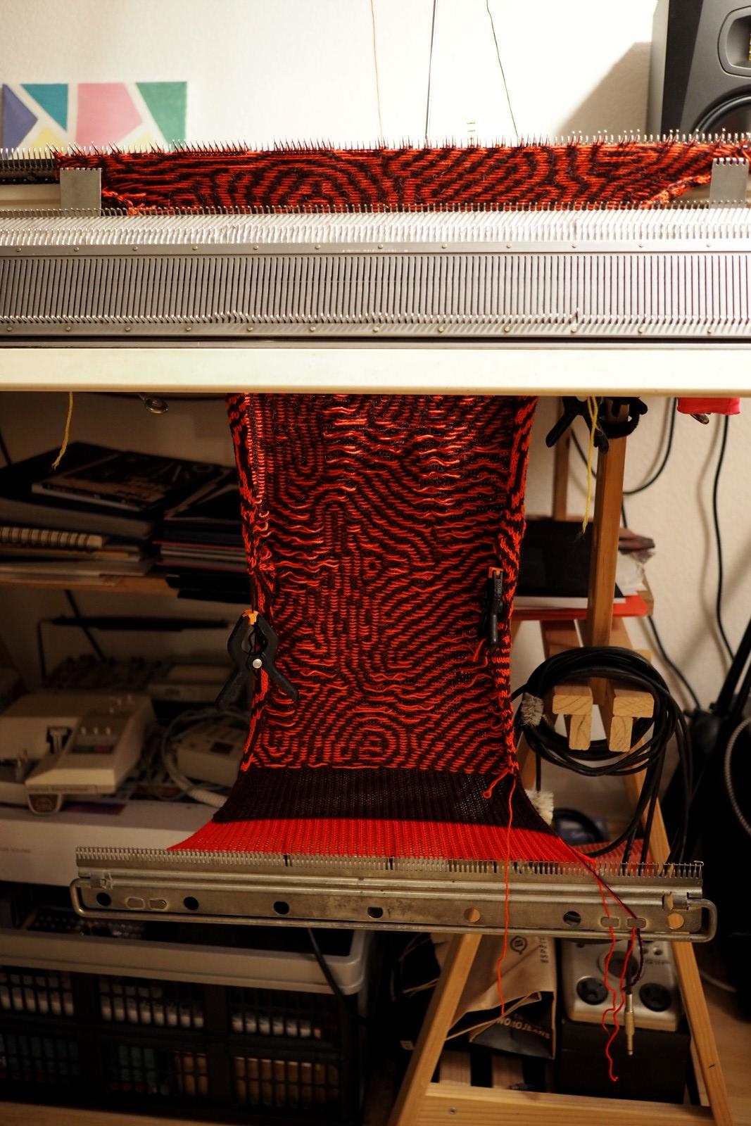 A piece of knitted fabric hanging on a knitting machine