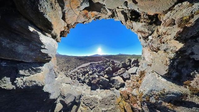 One of a series of photos showing a person hiking around a lava rock field in the Willamette National Forest of central Oregon, often observing distant mountains on the horizon, all under clear blue skies.