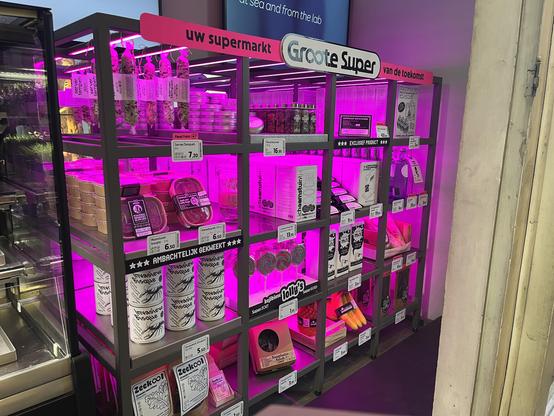 Display of various packaged food products on a purple-lit metal shelf in a supermarket, with multiple labels and price tags.