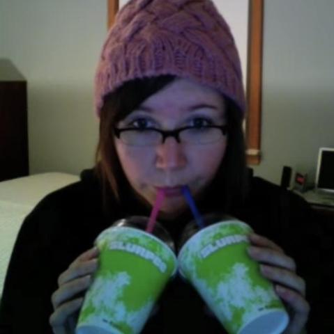Awkward girl wearing a pink knit cap while simultaneously drinking two slurpees.