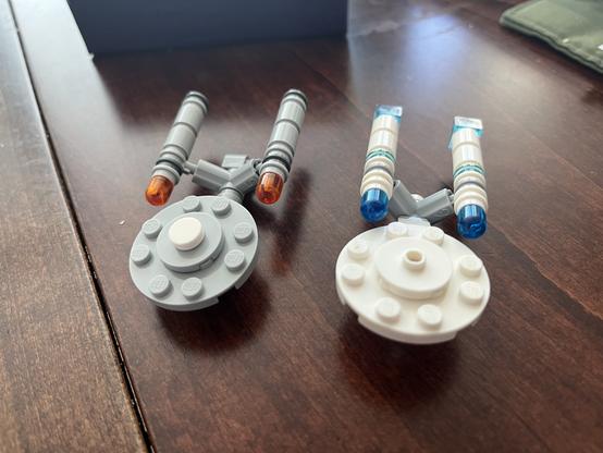 Two small Lego Enterprise models. One model is gray with orange-tipped engines, while the other is white with blue-tipped engines.