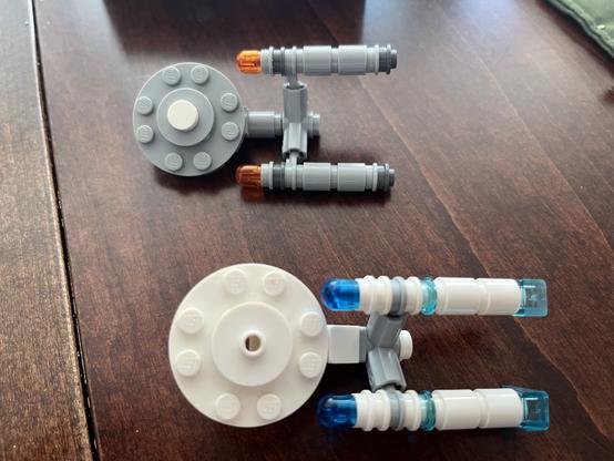 Two small Lego Enterprise models. One model is gray with orange-tipped engines, while the other is white with blue-tipped engines.
