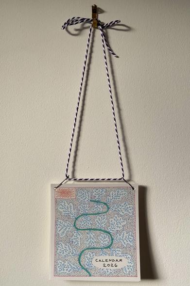 A calendar hanging from purple and white string on the wall. The cover of the calendar is illustrated with oak leaves.