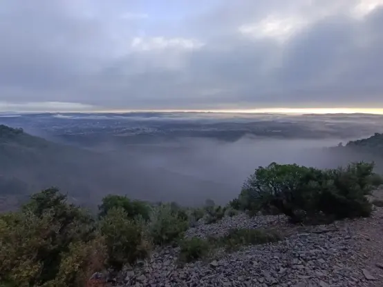 Sous un ciel nuageux, une large nappe de brume masque une plaine vue des hauteurs d'un massif.