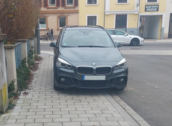 Schöner breiter Fußweg der von einem protzigen BMW der noch dazu viel zu nah an der Straßeneinmündung steht fast vollständig zugeparkt ist.