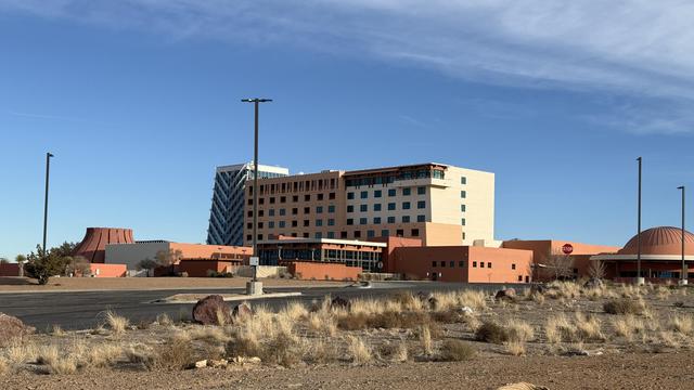 Photograph of the casino resort hotel I parked at overnight. This is mostly a back view; there are quite a few cars in the parking lot out front. Photo shows 10 and peach colored building approximately six stories tall with an ornate glass front surrounded by a bunch of salmon colored buildings in the foreground. closer in the foreground is a parking lot and an area of dirt with weeds. The sky is blue with light cirrus clouds.