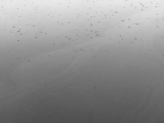 a still lagoon, looking like a flat rectangle gradiated from dark at the bottom to light at the top. raindrops lightly patter the surface
