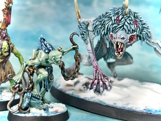 close up of one of the (greenish) ghouls trying to use a rusted hook to get hold of the bigger, meaner monster (probably about to loose that hand).