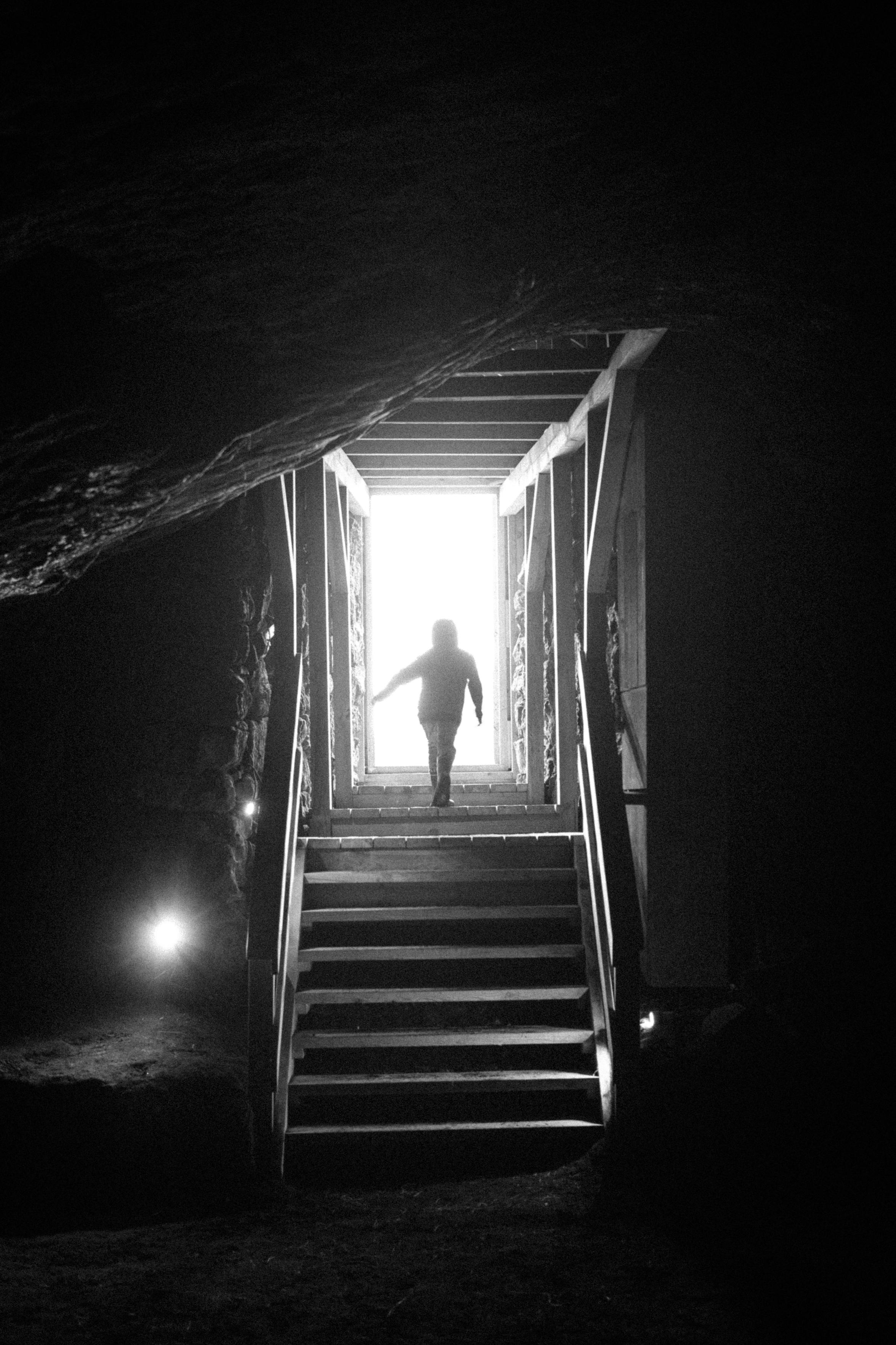 A child walks up the steps out of a dark cave, silhouetted against the bright light.