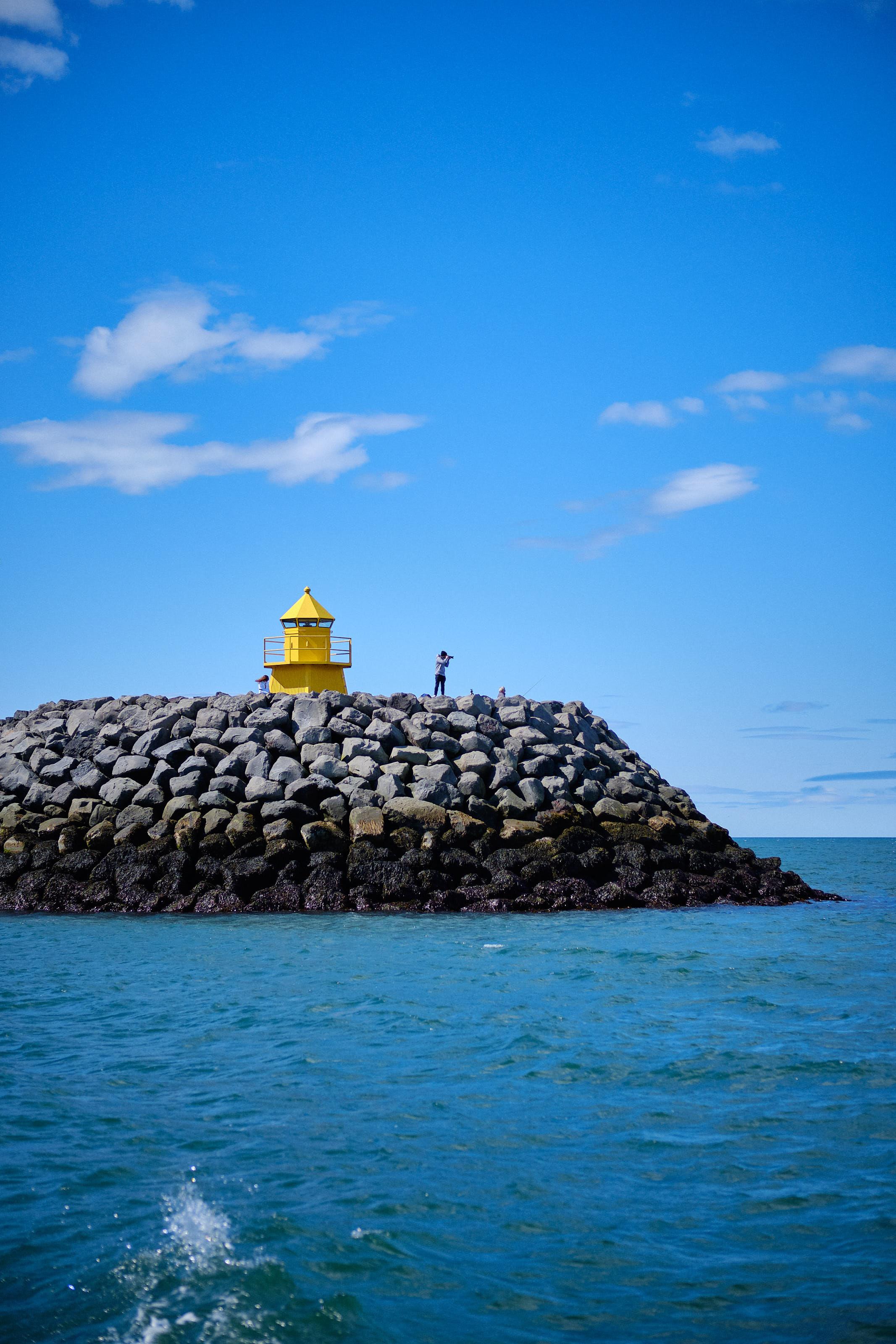 A very blue photo of a man on a pier, next to a small lighthouse-looking thing, taking photos with a big camera
