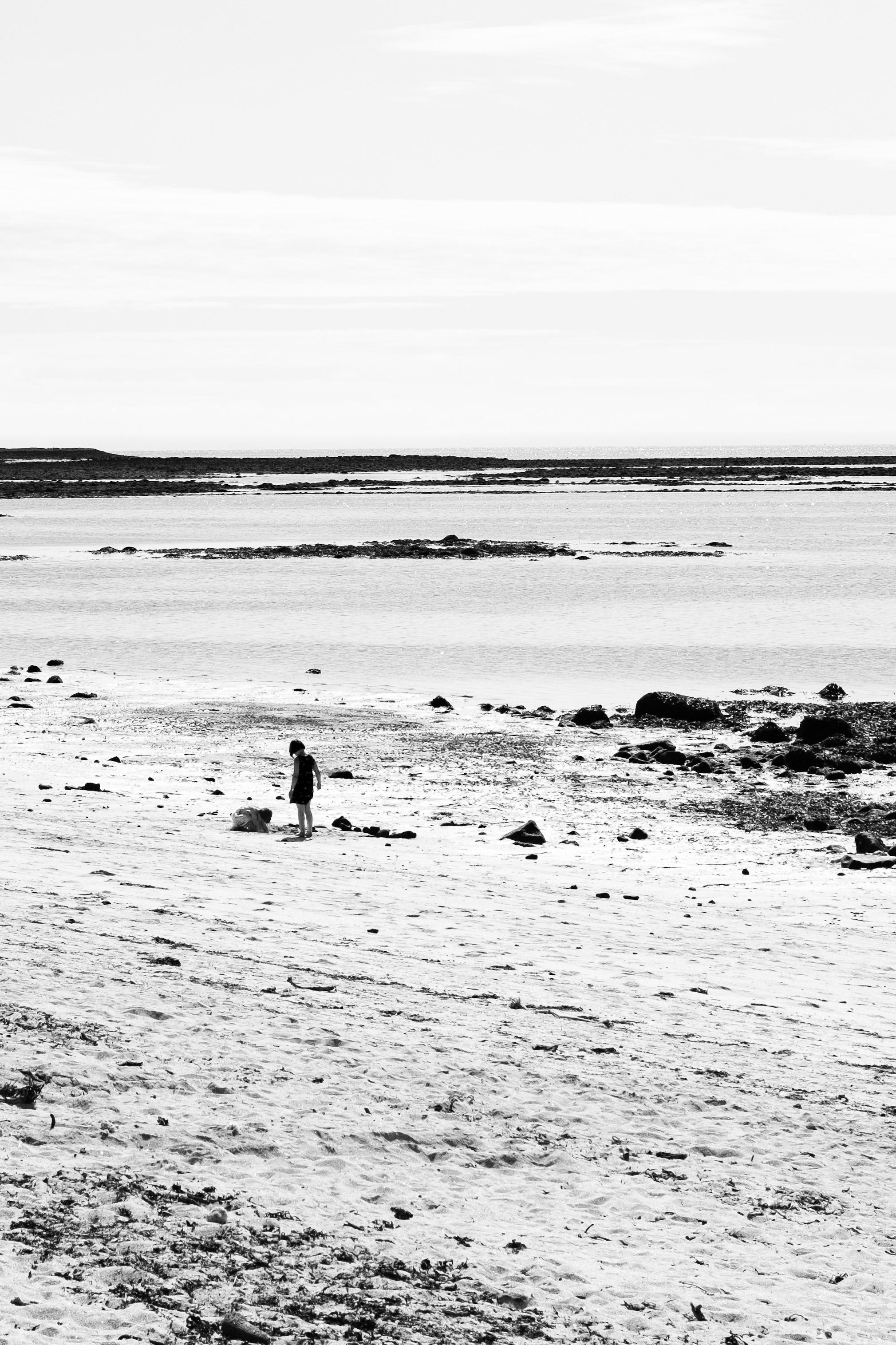 A very black and white photo of a beach, in the distance an unidentifiable child is playing.