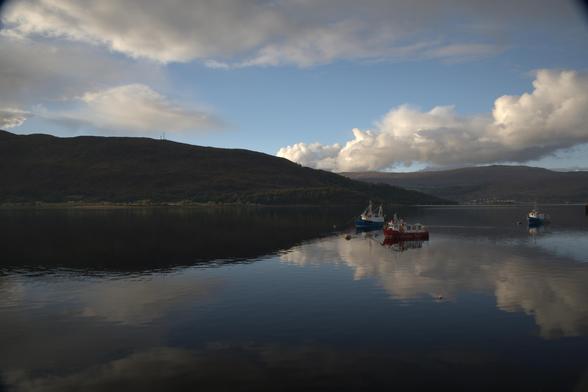 Boats moored on the loch at Fort William, the partly cloudy sky is reflected almost mirror-like on the still water