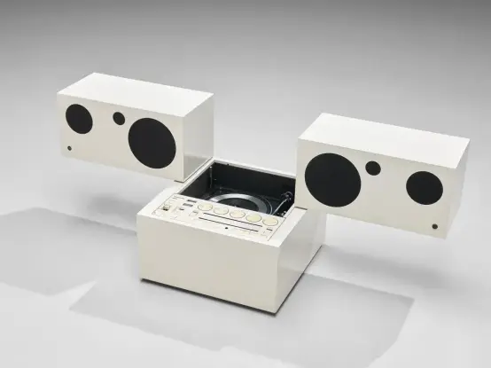 Almost entirely white stereo cube with two speakers that are mounted on the receiver. The speakers are suspended off to the sides with minimal overlap. There is a record player peeking out from the receiver. All of the buttons and dials are aligned in a single panel on the top surface.
