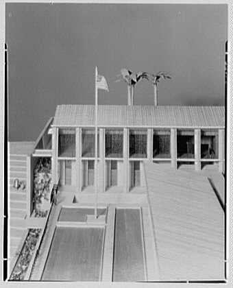 The image depicts a black and white photograph of an architectural model, representing the design for what appears to be a government building. The structure has multiple levels with rows of windows along its facade. Two flagpoles stand prominently in front of the main entrance. Pools or water features are visible at either end of a central walkway that leads up to the building's door. There is landscaping around these areas, including what looks like trimmed bushes and possibly flower beds.

The model shows an open concept with large glass windows allowing visibility into the interior spaces. The overall design reflects modernist architectural principles from mid-20th-century America. Given the context provided by additional information in Hare and Hatch (125 Broad St., New York City) and Gottscho-Schleisner, Inc.'s involvement as creators of this model, it is likely that this was a conceptual design for an embassy or consulate building.

The image's historical significance lies in the fact that it provides insight into mid-20th-century architectural trends and possibly American foreign policy during that time period. The exact location remains unknown but could potentially be related to political events surrounding Honduras IV around October 13, as mentioned alongside this model representation.