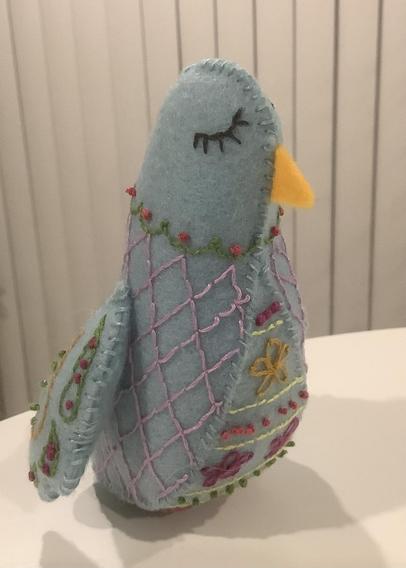 3/4 view of a light blue bird made of felt with various embroidery stitches to create the bird’s markings.