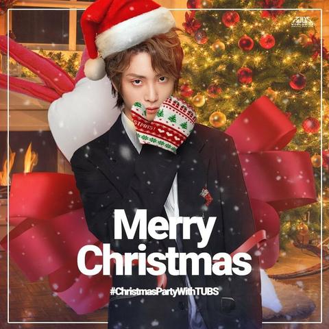 Yu Bin wearing a rumpled suit, a Santa hat, and a gigantic red bow apparently attached to his back. He is holding one hand, wearing a huge knitted Christmas mitten, up to his face and attempting to look sultrily at the camera over it.