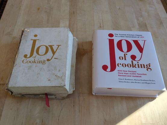 Two copies of Joy of Cooking cookbook side by side. The left one is from 1997 and is stained and tattered and has a broken binding, the second to the right is brand new.