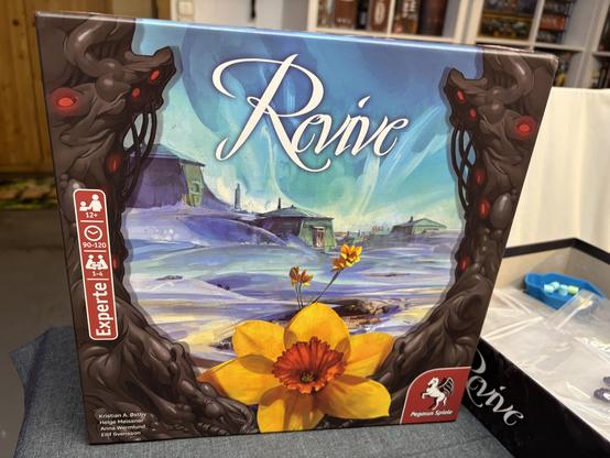 The image features a board game box titled "ReVive." The artwork showcases a surreal landscape with a flower in the foreground and dark, twisted structures on the sides. The box indicates it's for ages 12 and up, accommodates 1-4