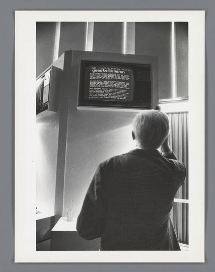 The image is a black and white photograph featuring an individual seated in front of a television set. The person appears to be focused on the screen, with their head slightly tilted downwards towards it. They have short hair that falls just above what could be seen as ears if they were visible from this angle, but we can't see them.

The TV is mounted at eye level and seems quite large in proportion to the individual's size compared to modern standards. It displays a screen with text which appears to be written in Dutch or a language using similar characters. The date "21-sep-83" suggests that this might have been taken on September 21, 1983.

The room is sparsely furnished; aside from the TV and what could possibly be an amplifier below it, there's little else visible in terms of decor or objects other than a faintly discernible bottle to the right side near the bottom edge. The curtains are drawn back slightly, allowing some natural light into the space.

The overall atmosphere feels quite dated with its vintage technology and monochrome aesthetic.