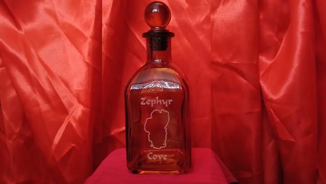 A perfume bottle inscribed with the outline of Lake Tahoe and the words "Zephyr Cove" in front of a red backdrop.