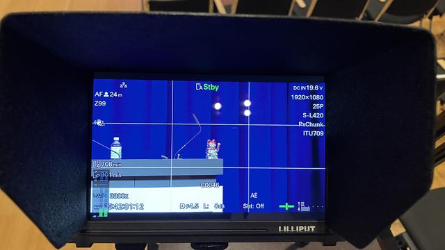 silberne winkekatze auf grauem pult im fokus der kamera. bild vom kontrollmonitor diversen technischen angaben.