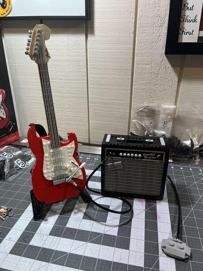 A completed Lego Stratocaster lego set. A red Stratocaster sits on a stand on the left and a Princeton Reverb amplifier sits on the right.