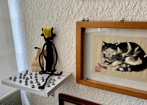 A pipe cleaner figure of a little gremlin and a lot of bean dust bunnies, sitting on a shelf next to my desk.