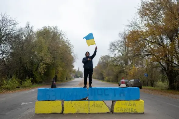 A local resident waves a Ukrainian flag at a former Russian checkpoint at the entrance of Kherson as local residents celebrate the liberation of the city, on Nov. 13, 2022. Ukrainians in the liberated southern city of Kherson expressed a sense of relief on Nov. 11, 2022, after months of Russian occupation