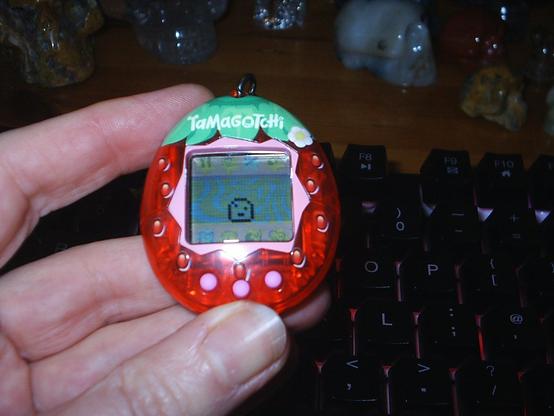 Gen 2 Tamagotchi virtual pet. The shell resembles a vibrant strawberry. On screen is a little pixel baby blob.