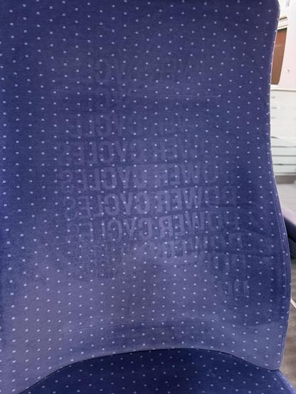 Foto der Rückenlehne eines DB-Zuges. In das Muster ist der mehrfache "POWER CYCLES"-Schriftzug von der Rückseite des 39C3-Merchs eingedrückt und als Muster zurückgeblieben.