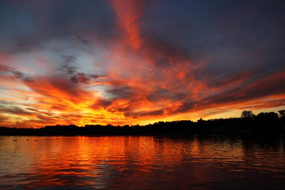 Sunset photo of yellow and orange clouds stretching out over the horizon with the light reflected below in a lake.