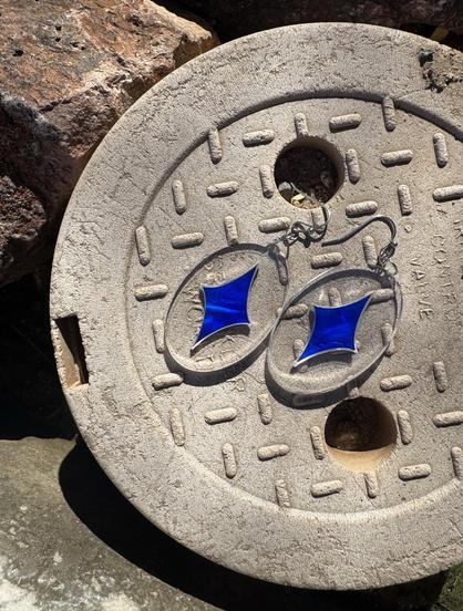 laser cut earrings on outdoor valve cover. the earrings are marbled blue stars inset in clear acrylic, creating a faux floating effect