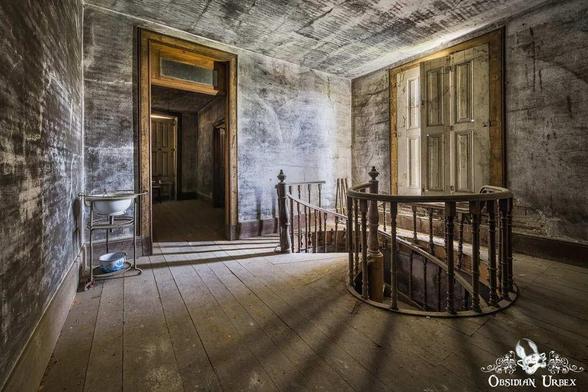 An aged interior with a spiral staircase and open doorway shows deterioration. The scene has peeling paint, weathered wood