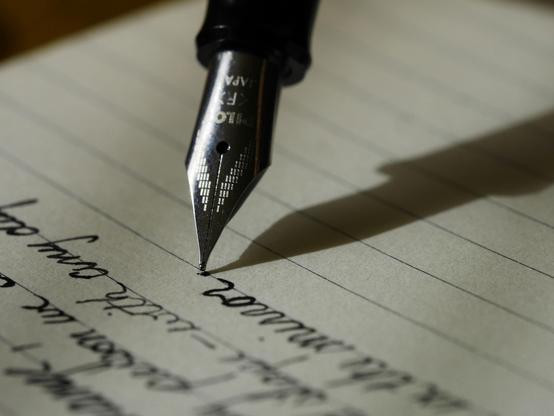 A black fountain pen writes in cursive on a lined page.
