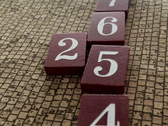 Spielsteine mit Ziffern, eine 2 liegt links neben einer vertikalen Reihe mit 4, 5 und 6. Man sieht eine 25 wobei die 6 anfängt die 5 nach unten zu verdrängen